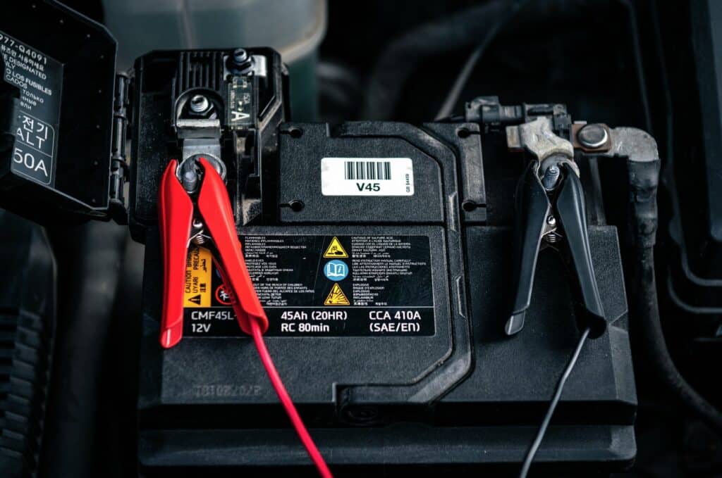 En rød og svart klemme som er festet på pluss- og minuspolene på et 12-voltsbatteri i bil.