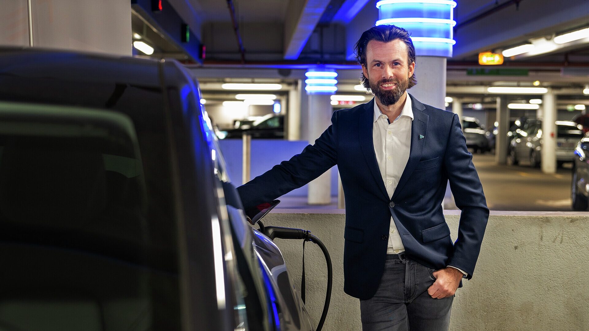 Smilende mann ved siden av elbil.